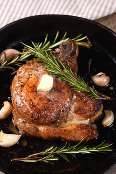 Pork cutlet on the bone in a piece of butter with garlic and rosemary in a frying pan 