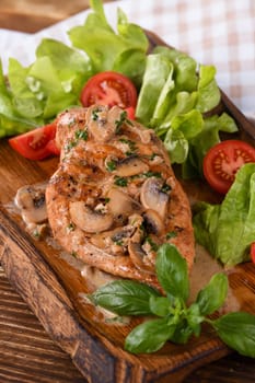 Chicken breast with mushroom sauce and vegetables on a wooden plate