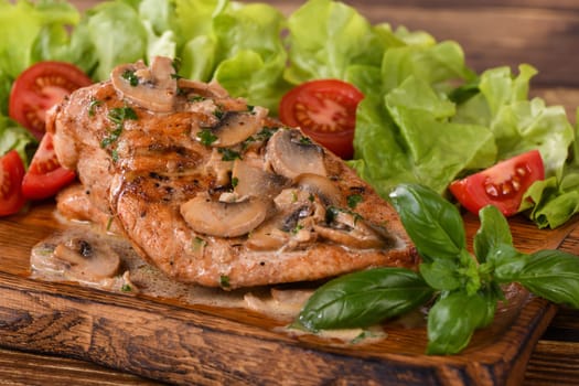 Chicken breast with mushroom sauce and vegetables on a wooden plate
