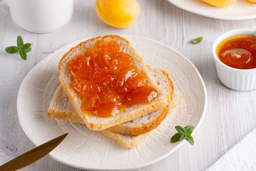 Apricot jam on bread in a white plate and a jar of apricot jam.
