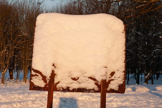 Information board covered with snow, close-up against the background of a winter forest.