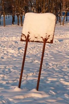A wooden, snow-covered, leaning information sign in the forest.