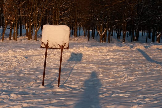 Information board covered with snow in a winter forest in sunny weather.