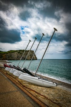 catamarans or boats with masts in a row on a beach in Normandy with the elephant rock of the chalk cliffs of Etretat in normandy