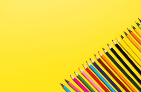 Set of multi-colored pencils on a yellow background.