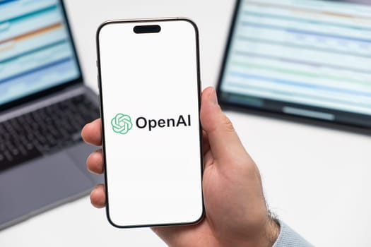 PRAGUE, CZECH REPUBLIC - JANUARY 21 2024: Open AI logo on the screen of smartphone in mans hand on the workplace background.