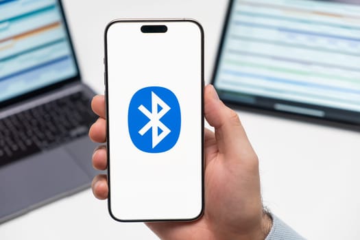PRAGUE, CZECH REPUBLIC - JANUARY 21 2024: Bluetooth logo on the screen of smartphone in mans hand on the workplace background.