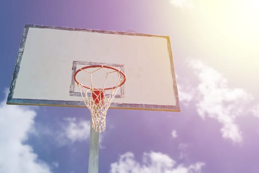 Orange basketball rim with white net and wooden backboard against blue sky