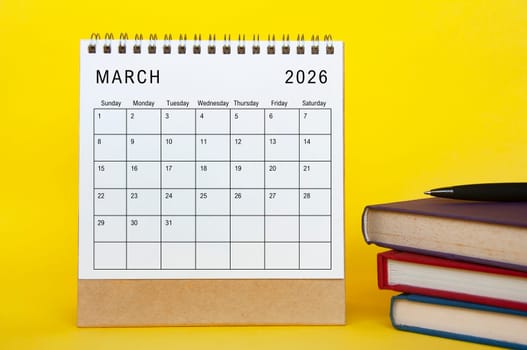 March 2026 calendar with yellow cover background and books. New month and calendar concept
