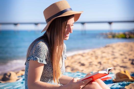 Woman sitting on the beach wearing hat reading a book,with the sea in the background