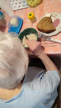 elderly gray-haired woman eats at the table, sits with her back turned, food cooking. High quality photo
