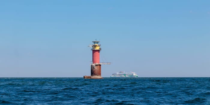 Gulf of Finland, Estonia, June 28, 2024 -A lighthouse in the Baltic Sea near Tallinn and ferry Tallink from Helsinki. Blue sky, clouds, waves, sea. Banner with copy space