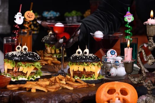 A witch's hand takes a Witch cocktail with eyeballs in a martini glass from the Halloween party table.