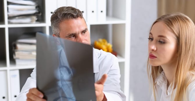 Portrait of doctor talking with colleague about leg x ray result, doc need advice from coworker. Recovery, medicine, healthcare, injury, treatment concept