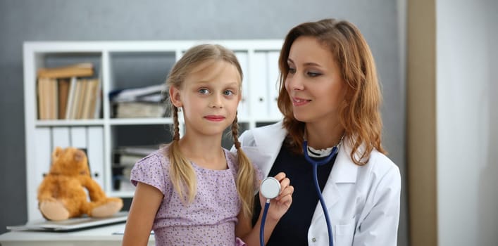 Portrait of pediatrician doctor with child on lap, kid play with stethoscope tool, happy kid on appointment, health. Medicine, childhood, checkup concept