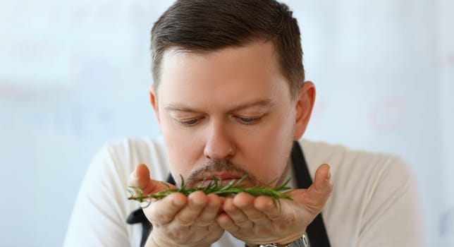 Portrait of professional chef smell twig of rosemary, herb add to dish, better taste with greenery. Cooking as hobby, enjoy delicious food. Eating concept