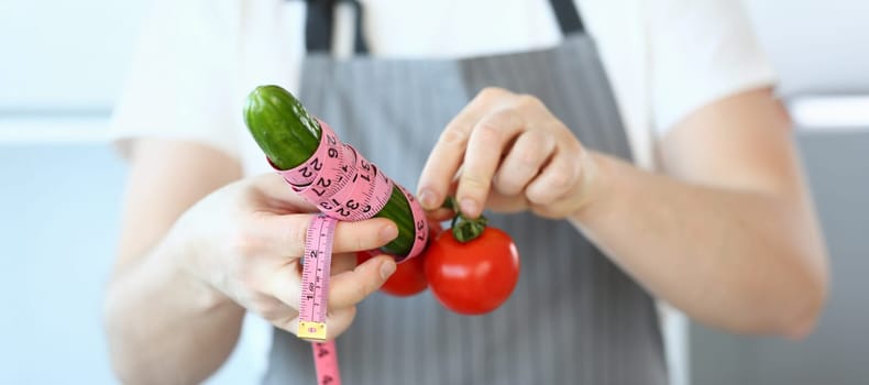 Close-up of person hold cucumber and tomatoes with measure tape around, create male organ with vegetables. Sport nutrition, health, fun, humour concept