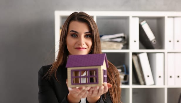 Portrait of woman realtor hold miniature toy house in hand, symbol for real estate. Sale or rent construction, apartment and housing. Accommodation concept