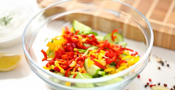 Close-up of delicious fresh salad with mellow vegetables, cucumber and pepper ingredients. Meal served in glass bowl. Cooking, organic, healthy concept