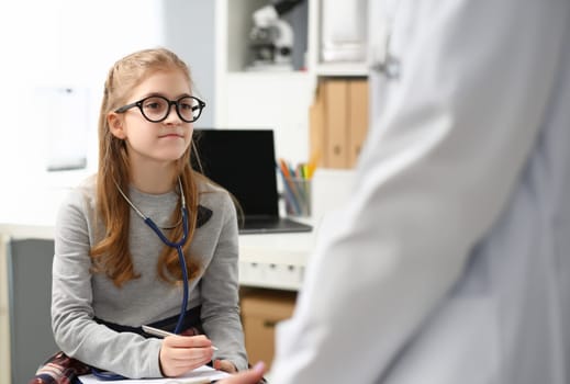 Portrait of young child wants to be doctor, write advices on paper, wear stethoscope equipment on neck. Education, knowledge, future medical worker concept