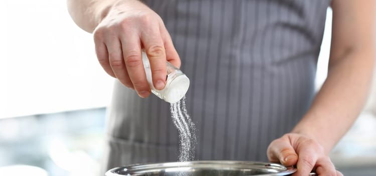 Close-up of professional cook hold saltcellar and add salt to soup, chef follow recipe, nutritious meal. Cooking, hobby, professional, homemade concept