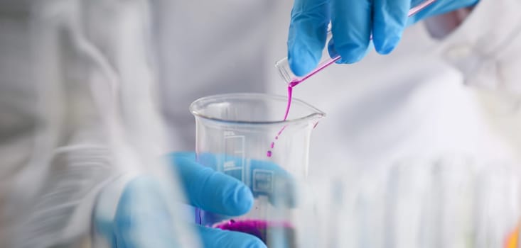 Close-up of scientist pour pink liquid from flask in medical chemistry laboratory. Chemist experiment with formula. Science, discovery, testing concept