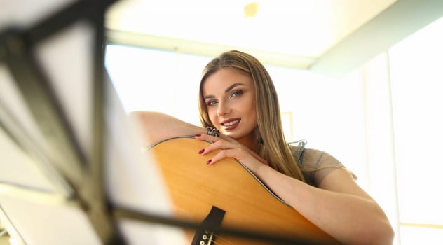 Portrait of inspired music composer, cute girl play on guitar, creative artist. Note on music stand in front. Solo, musical performance, rehearsal concept