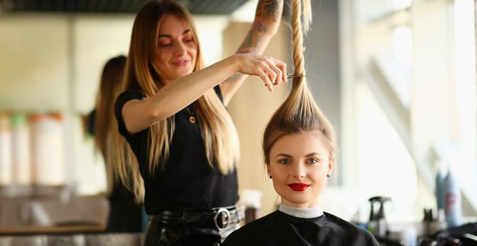 Portrait of hairdresser holding long lock of hair and going to cut length with scissors. Radical image change, dye hair. Beauty salon, barbershop concept