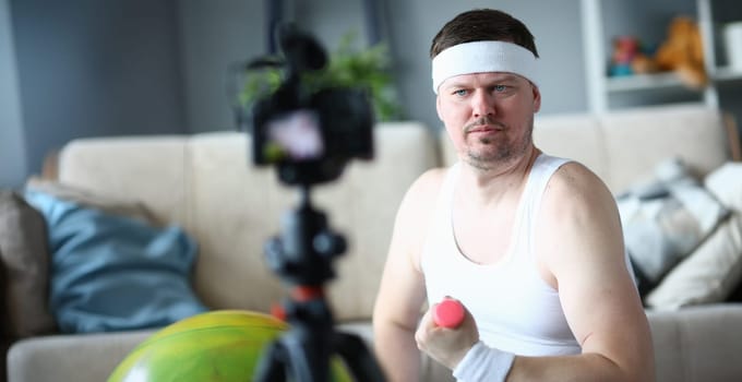Portrait of middle aged man training with dumbbells, record on videocamera. Sportsman filming exercise or full course for followers. Blogger, sport concept