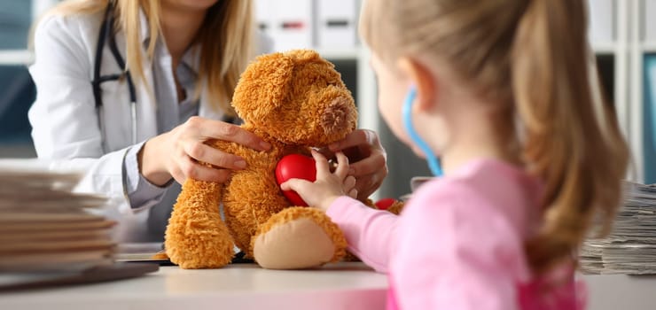 Portrait of little girl touch heart of stuffed teddy bear, listen with stethoscope, check heartbeat. Future doctor, medicine, childhood, cardiology concept