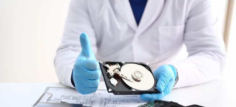Close-up of man in uniform hold disassembled hard drive from computer, hdd and reader, show thumbs up. Fixed part of computer device. Technology concept