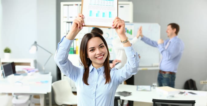 Portrait of woman lift document over head, celebrate good deal, beneficial agreement. Well done, good job, startup, teamwork, success, work party concept