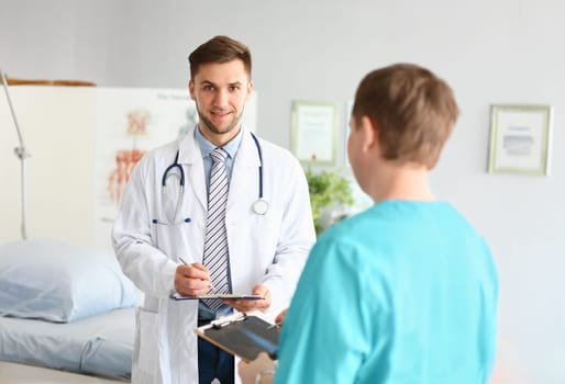 Portrait of head doctor in medical gown hold patient medical history, intern write prescription for client. Medicine, hospital, emergency, help concept