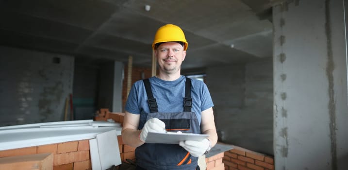 Portrait of worker hold clipboard and write down consumable materials for renovation. Foreman wear uniform and helmet. Construction works, project concept
