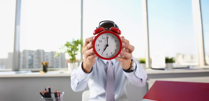 Close-up of person hold red clock with arrows on seven oclock in morning, time to start work. Start new day, being productive, office view. Wakeup concept