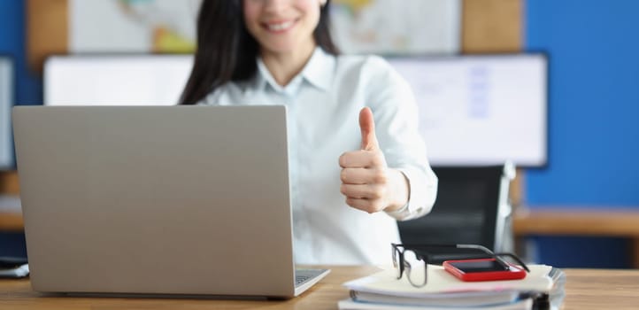 Close-up of office clerk showing thumbs up gesture working on laptop. Smiling employee express joy, good job, support business. Corporate, office concept