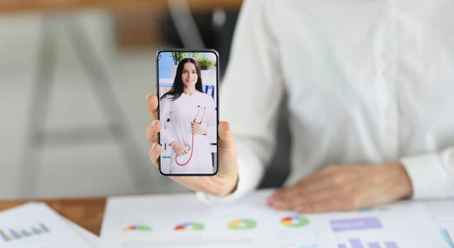 Close-up of woman office worker show smartphone with doctor woman on screen, change qualification. Brave enough to change profession. Retraining concept