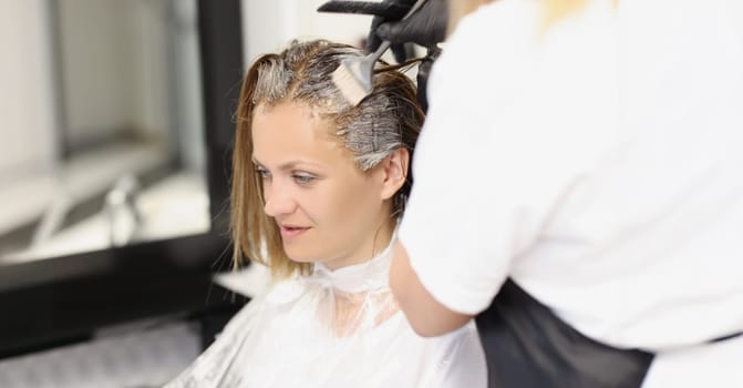 Portrait of hair master apply dye colour on hair with special tool. Client enjoy beauty procedure. Wellness, beauty salon, self care, barbershop concept
