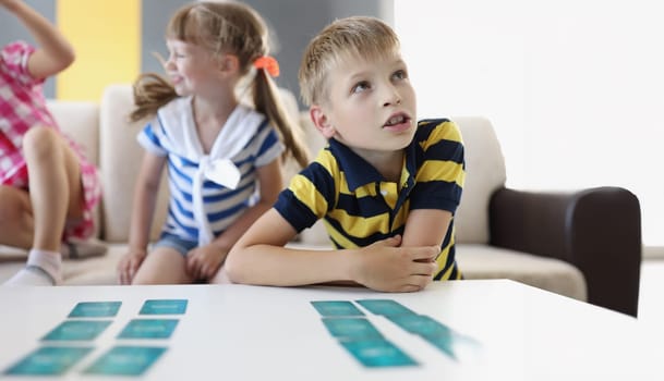 Portrait of kid friends playing card game on table at home, involved in development. Funny pastime for children on holiday. Childhood, fun, weekend concept