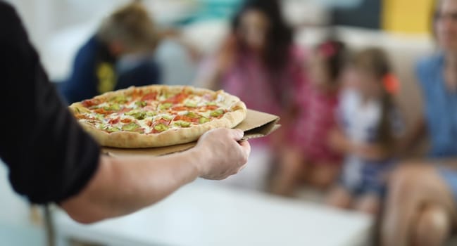 Close-up of man bring hot big pizza with stuffing and sauce. Smelly pizza with cucumber and cheese, order snack. Fast food, takeaway, hunger, party concept