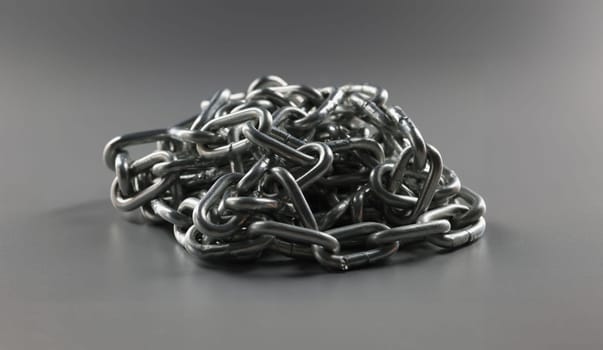Close-up of grey chain folded in heap, steel metal iron chain on grey surface. Solid chain tangled in mess. Locking equipment, fixation instrument concept
