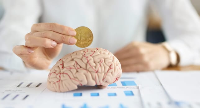 Close-up of businesswoman holding bitcoin coin in front of human brain. Smart part of human body, create idea, find ways to earn. Intellect, invest concept