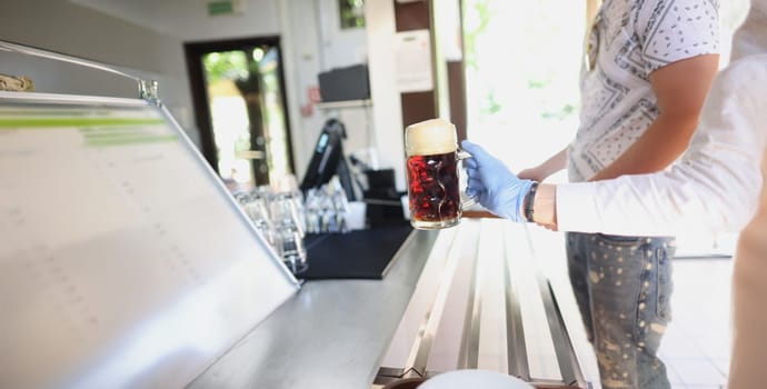 Close-up of waiter give glass with beer to client in protective glove, prevent covid spread. Bar, cafe or restaurant ground. Order, drink, beverage concept