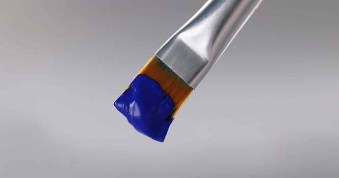 Close-up of brush with blue greasy oil paint on tip, professional equipment for drawing on grey background. Masterpiece, art, creativity, artistry concept