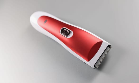 Top view of electric hair machine for trimming hair, red colour design on grey surface. Equipment to correct or create hairstyle. Hairdresser tool concept