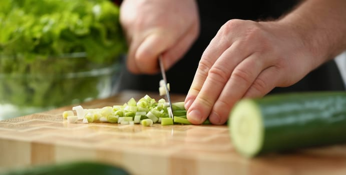 Close-up of professional chef cut spring onion with sharp knife on cutting board. Person follow delicious new recipe. Cooking, food, meal, homemade concept