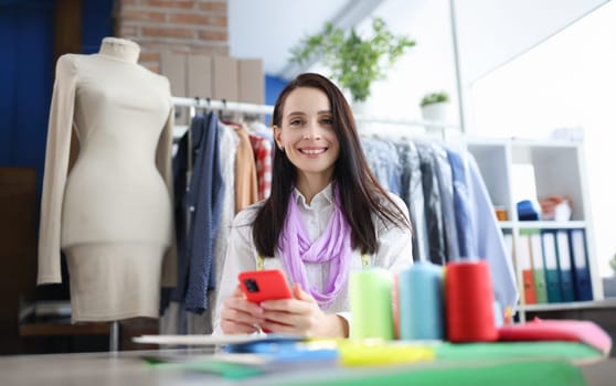 Smiling blooming woman holding smartphone at workplace. Profession fashion stylist concept