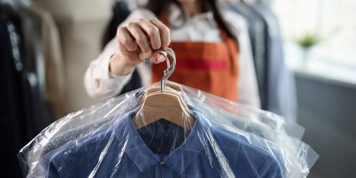 Professional worker keeps clean clothes on hangers. Laundry and dry cleaning services concept