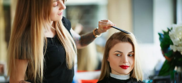 Portrait of hairdresser using comb to brush clients hair, woman on appointment in salon. Professional master in beauty center. Wellness, barbershop concept