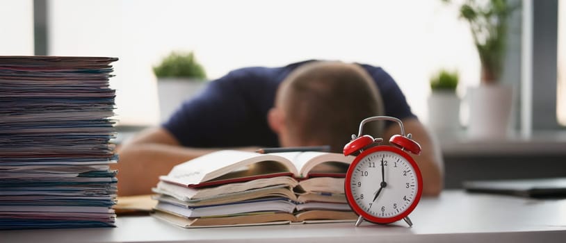 Close-up of tired student take nap behind pile of textbooks on table. Sleepy man resting during education after sleepless night. Despair, deadline concept